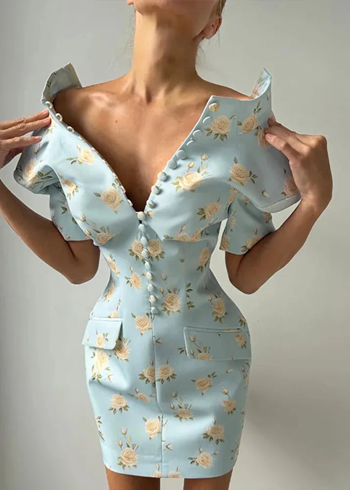A woman wearing a light blue off-the-shoulder bodycon mini dress with a beige and green floral print, featuring a deep V-neckline with decorative buttons and flap pockets.