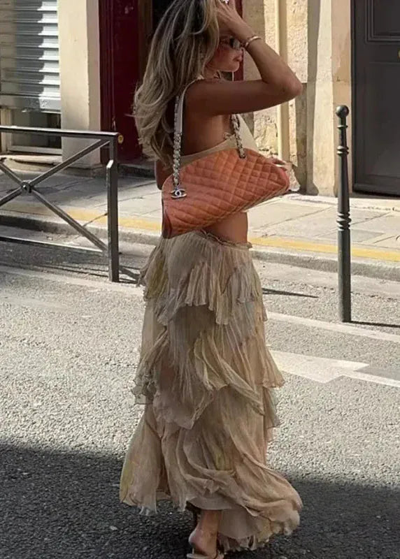 Woman in a beige ruffled dress holding a Chanel handbag on a city street.