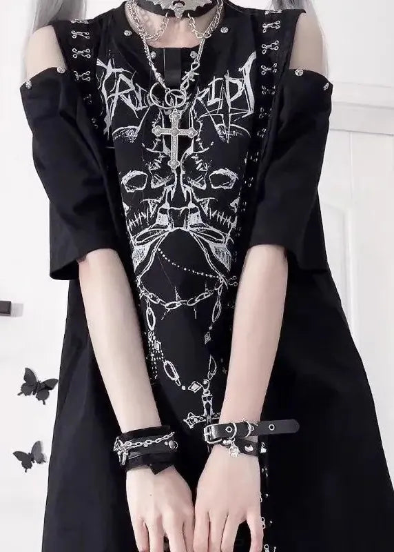 Person wearing a black outfit with white skull and crossbones design, standing against a white wall.