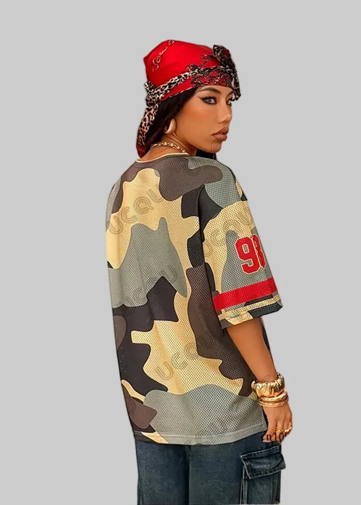 Person wearing a camouflage jersey with red accents and a red bandana, standing in front of a white wall with 'UCQU' branding.