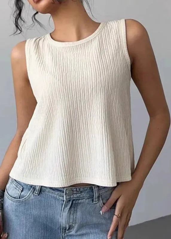 A woman wearing a sleeveless, ribbed-knit crop top in cream/off-white paired with light-wash blue jeans, shown from the chin down against a plain gray studio background.