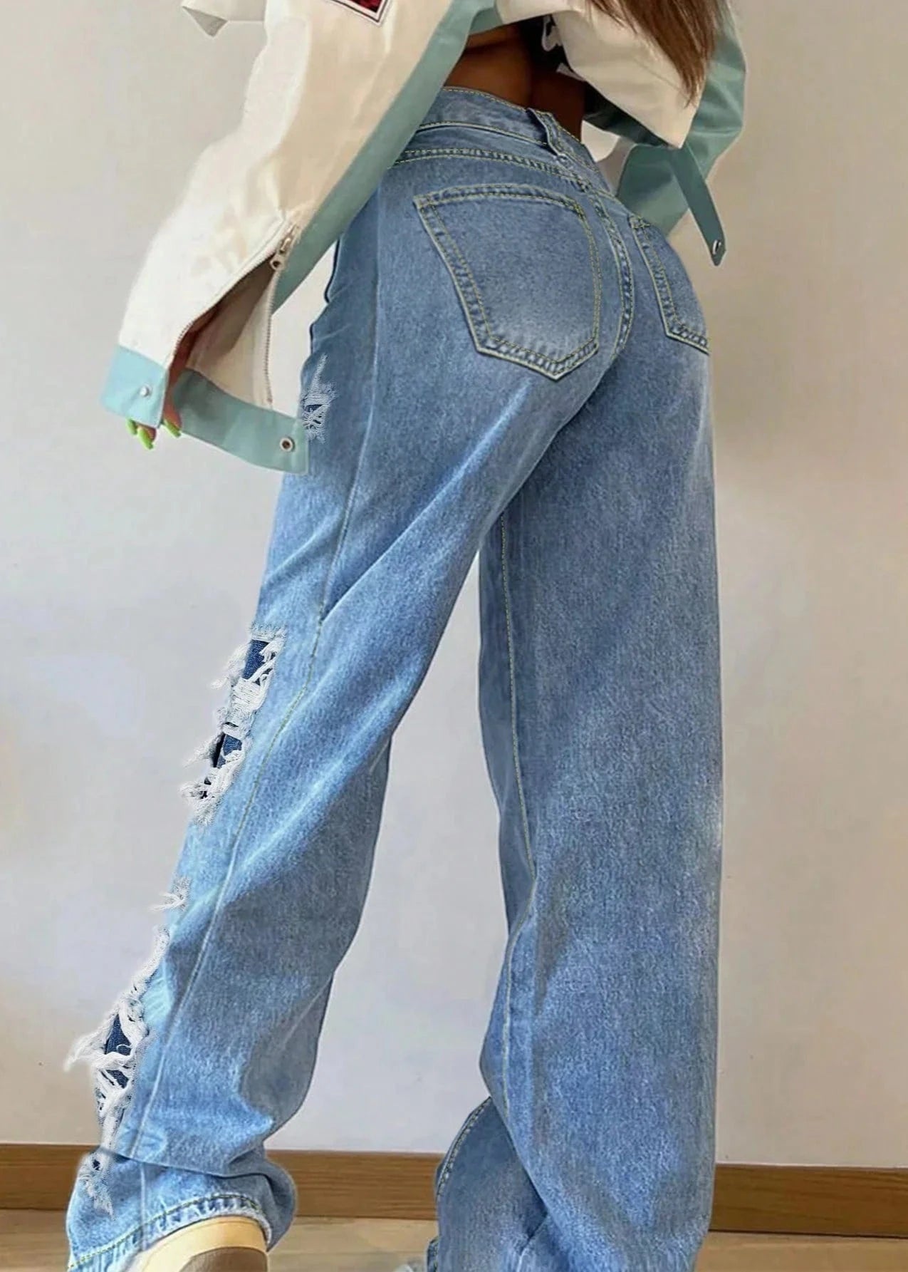 Person wearing light blue jeans and a white jacket with green accents on a plain background