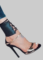 Black lace-up high-heeled sandal with gold accents on a light blue background
