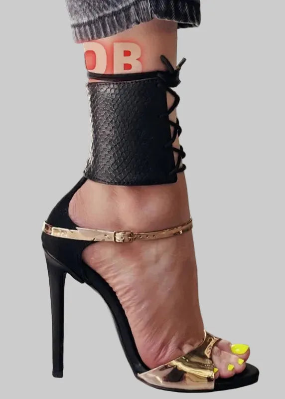 Black high-heeled shoe with gold accents worn by a person on a light gray floor.