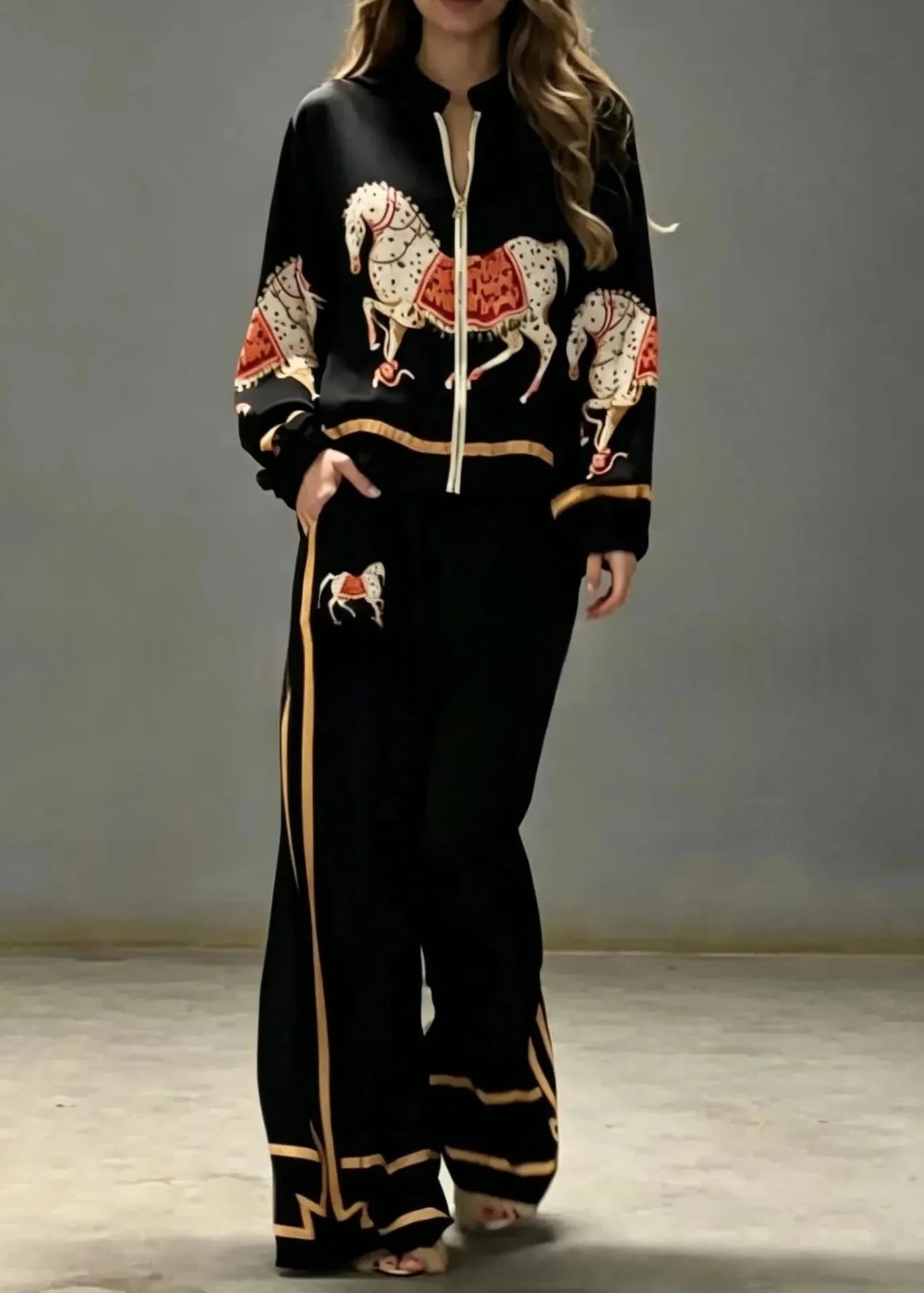 A woman modeling a black two-piece tracksuit featuring embroidered horse motifs in white, red, and gold, with gold piping details on the sleeves and wide-leg pants.