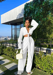 Woman in a white outfit standing on a rooftop with greenery and cityscape in the background