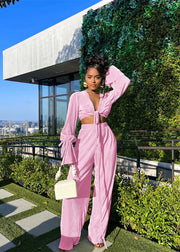 Woman in a pink outfit standing on a rooftop with greenery and cityscape in the background