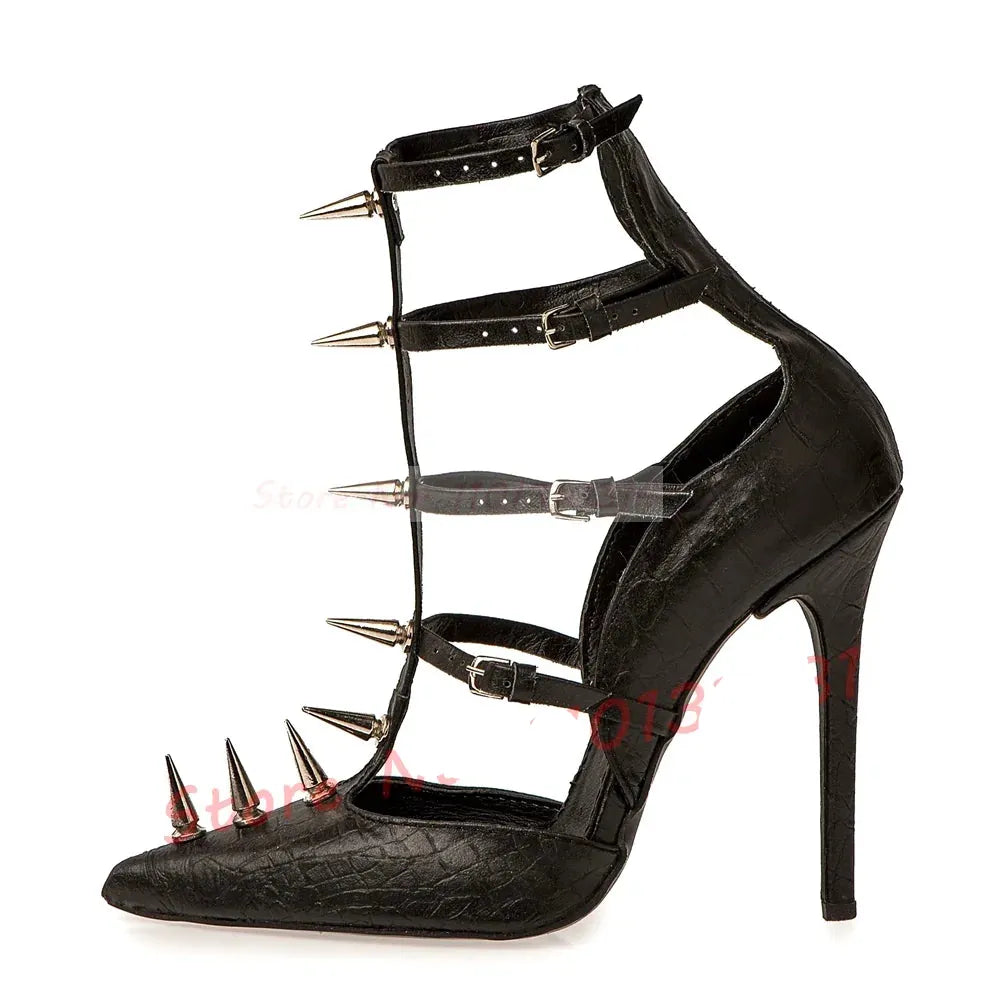 A single black high-heeled shoe with a pointed toe, stiletto heel, and multiple wraparound ankle straps topped with metal spikes. The shoe has a crocodile-embossed texture and is photographed on a plain white background.