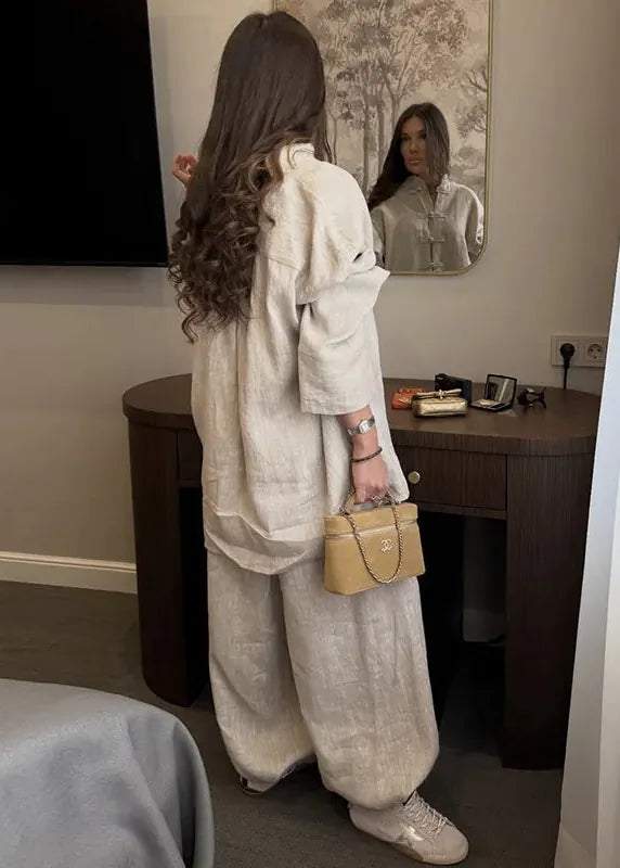 Woman in a beige outfit standing in front of a mirror in a room with a desk and television.