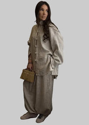 Woman in a beige outfit standing in a room with a mirror and desk.