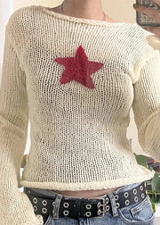 Beige sweater with a red star design worn by a person, with a blurred background.