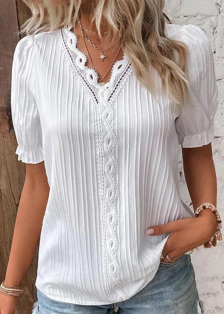 Woman wearing a white blouse with lace details against a wooden and white brick wall.