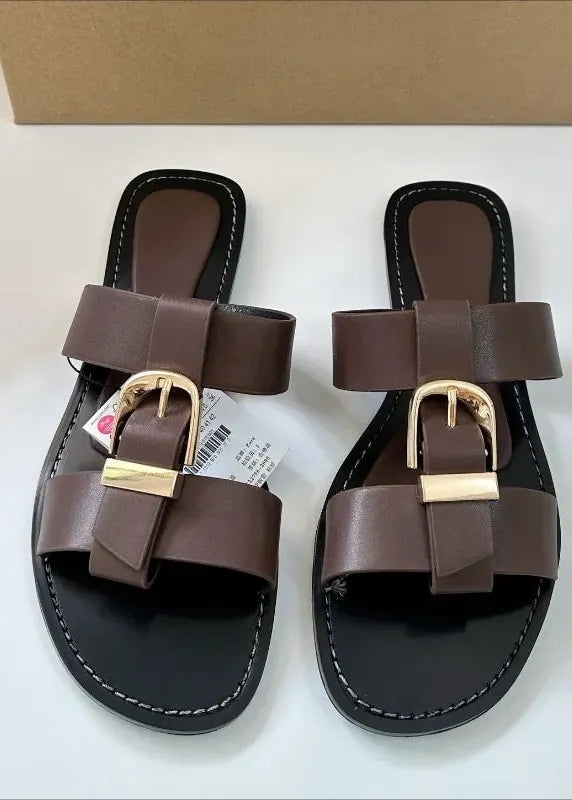 Pair of brown sandals with gold buckles on a white surface.