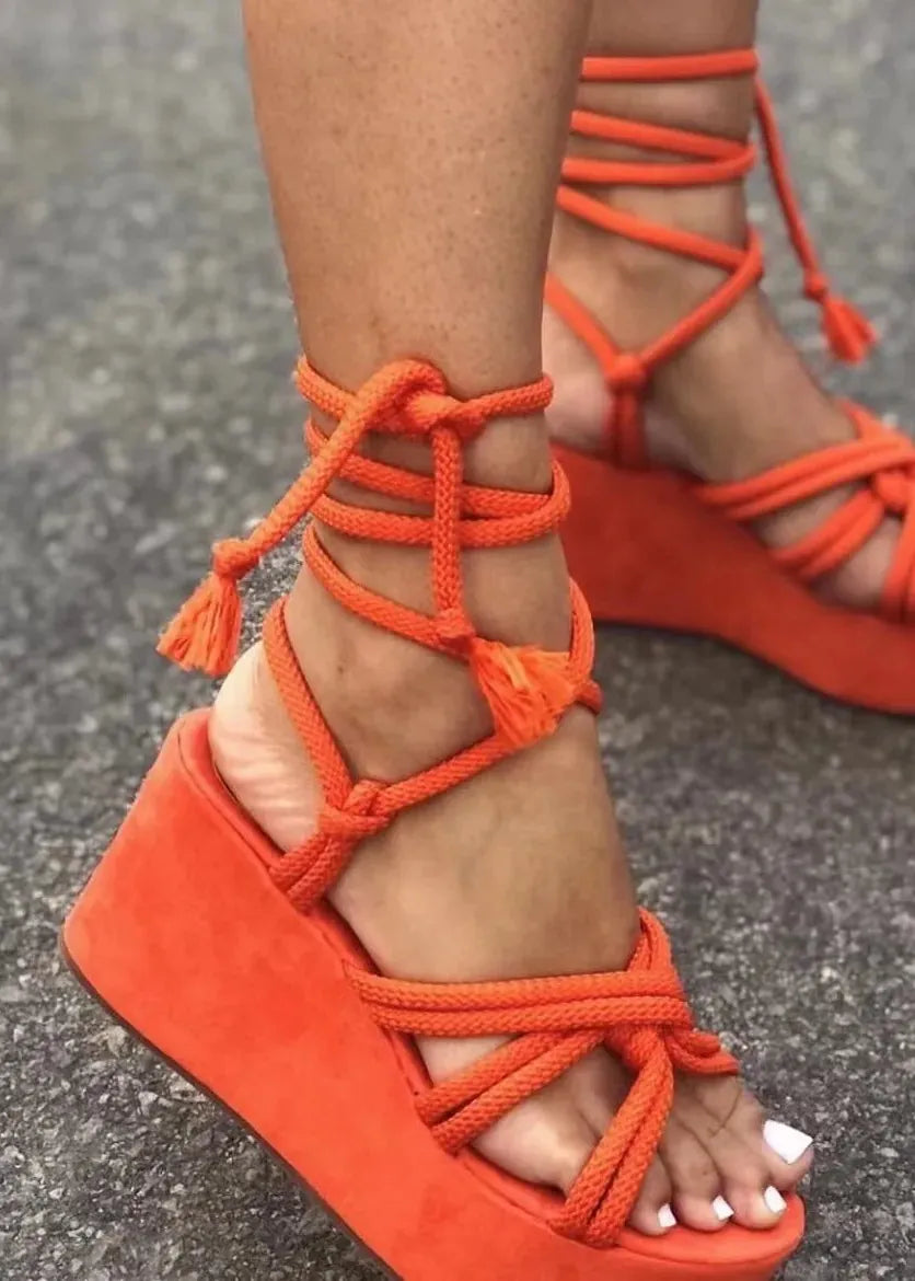 Orange wedge sandals with rope detailing on a gray pavement background