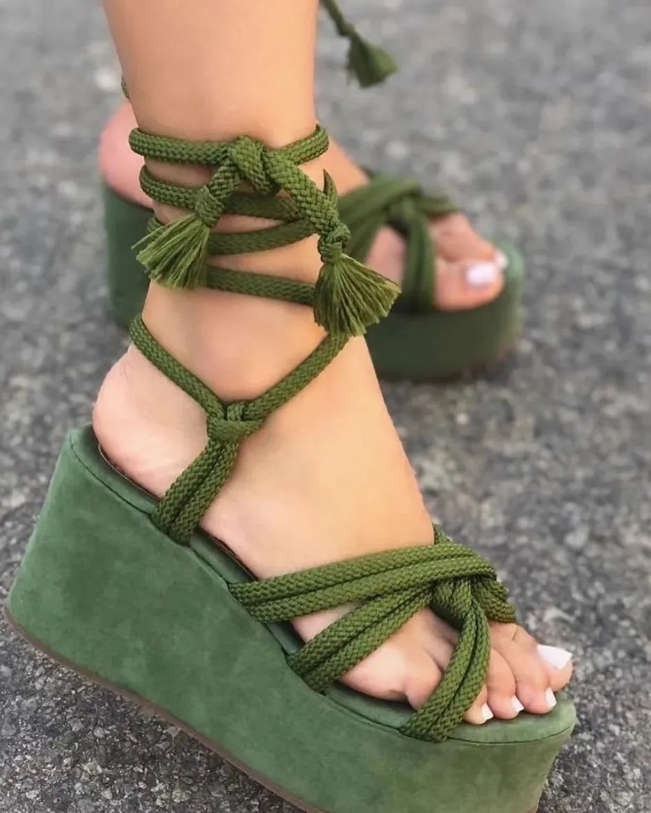 Green wedge sandals with braided straps on a gray pavement background