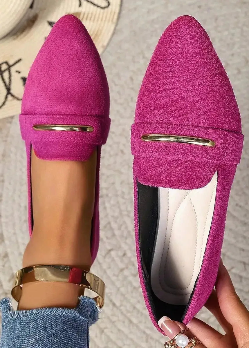 Pink loafers with a gold buckle held by a hand on a textured surface.