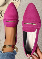 Pink loafers with a gold buckle held by a hand on a textured surface.