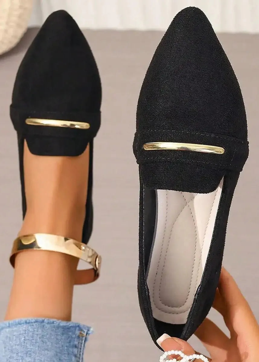 Black pointed-toe shoes with gold accents held by a person wearing gold bracelets.