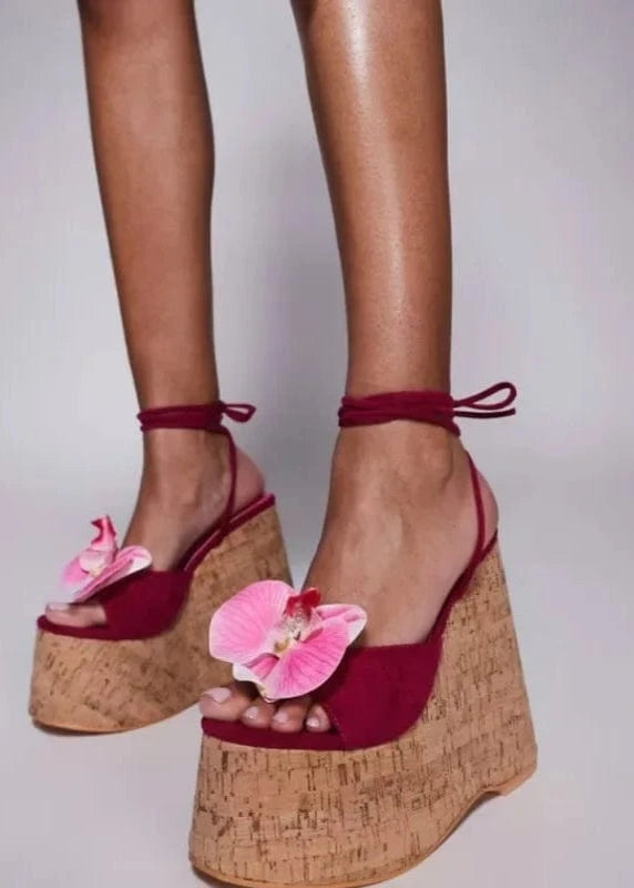 Red wedge sandals with pink flowers on cork soles against a neutral background