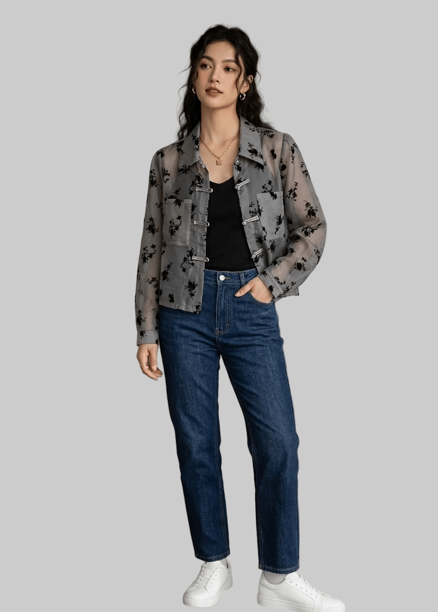 Woman wearing a gray floral jacket, black top, blue jeans, and white sneakers in an indoor setting.