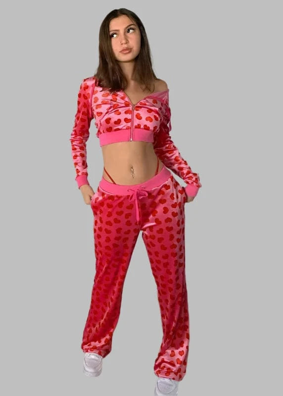 Woman wearing a pink and red polka dot tracksuit against a plain wall.
