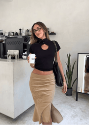 Woman in a black top and beige skirt holding a coffee cup in a modern cafe.