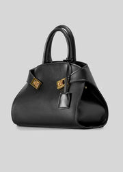 A black leather handbag with structured curved sides, dual top handles, and gold-tone hardware accents, photographed on a plain light gray background.