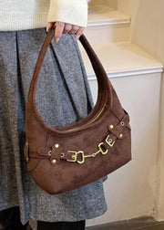 A person wearing a cream knit sweater and a gray wool skirt carries a brown suede shoulder bag with gold-tone hardware and horsebit details, standing indoors near white stairs.