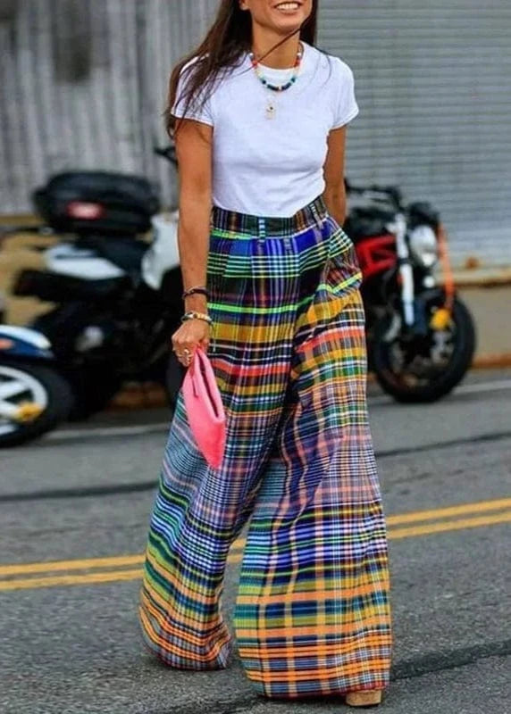Person wearing colorful plaid pants and a white shirt on a street with motorcycles in the background.