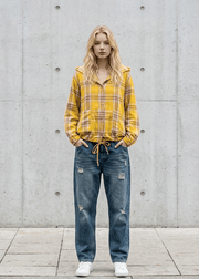 Person wearing a yellow plaid shirt and blue jeans standing against a gray concrete wall with 'arvin' branding.