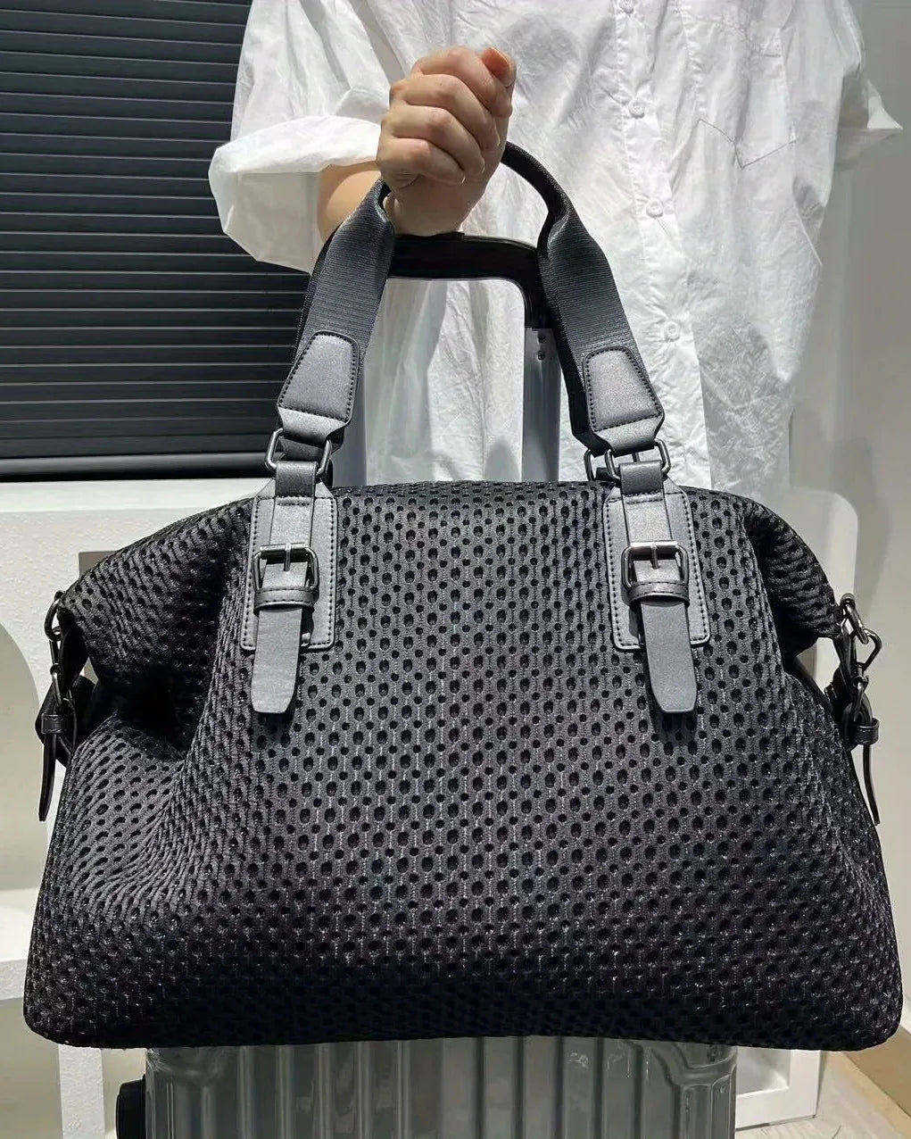 Black textured handbag held by a person wearing a white outfit.