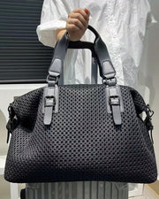 Black textured handbag held by a person wearing a white outfit.