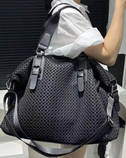 Person holding a black perforated handbag with a white shirt.