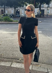 Woman in a black dress with embellishments standing on a street.