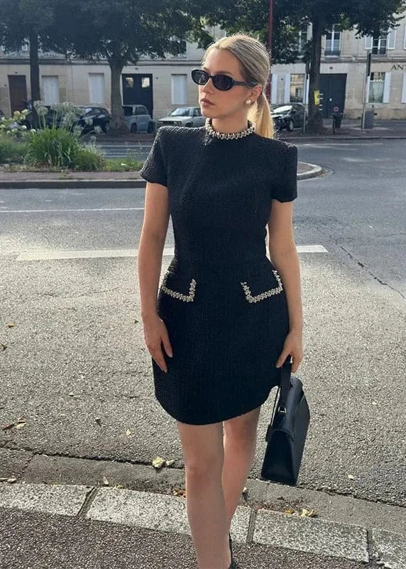 Woman in a black dress with embellishments standing on a street.