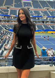 Woman in a black dress standing in an empty stadium with a tennis court in the background