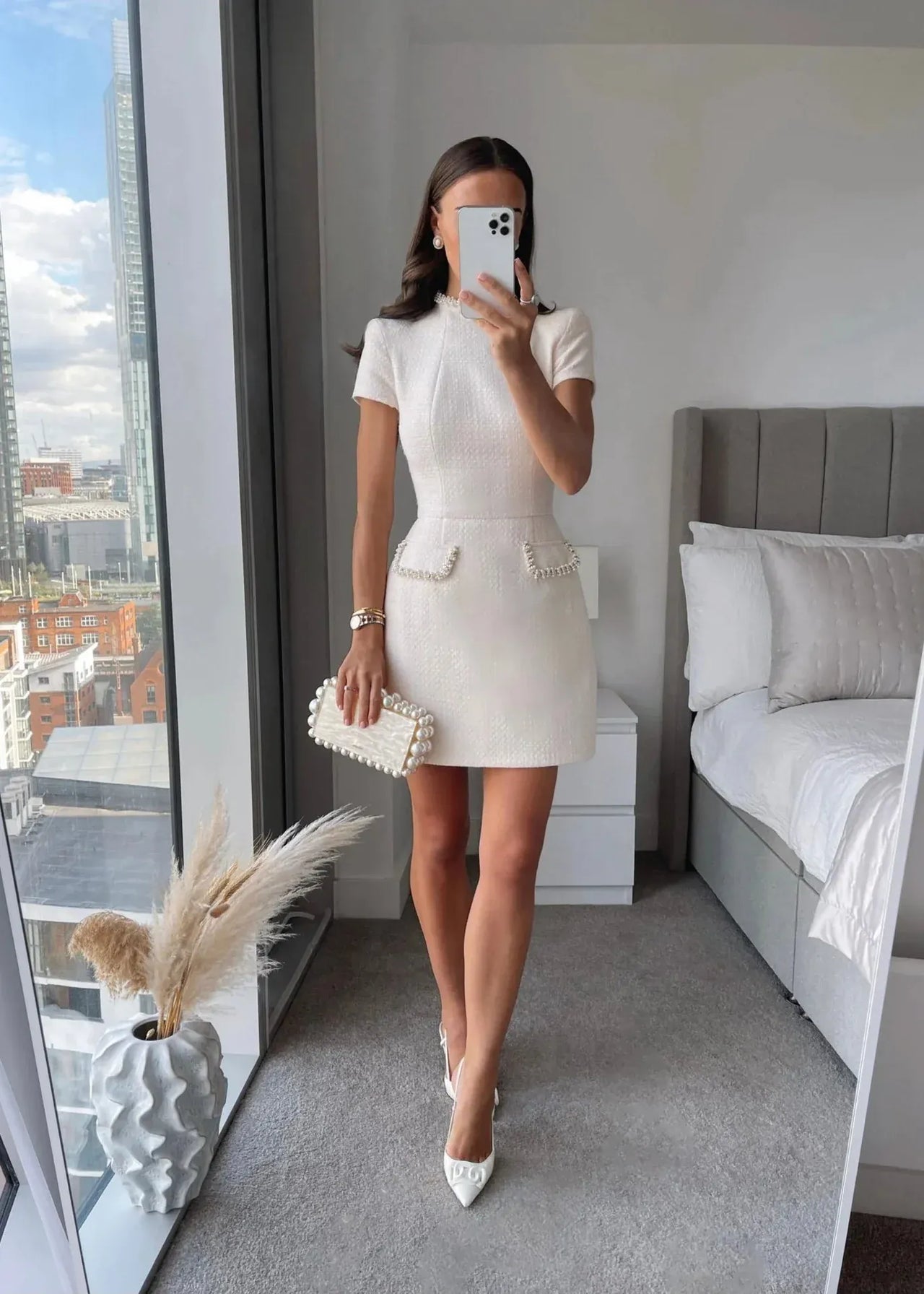Woman taking a mirror selfie in a white dress in a modern bedroom.