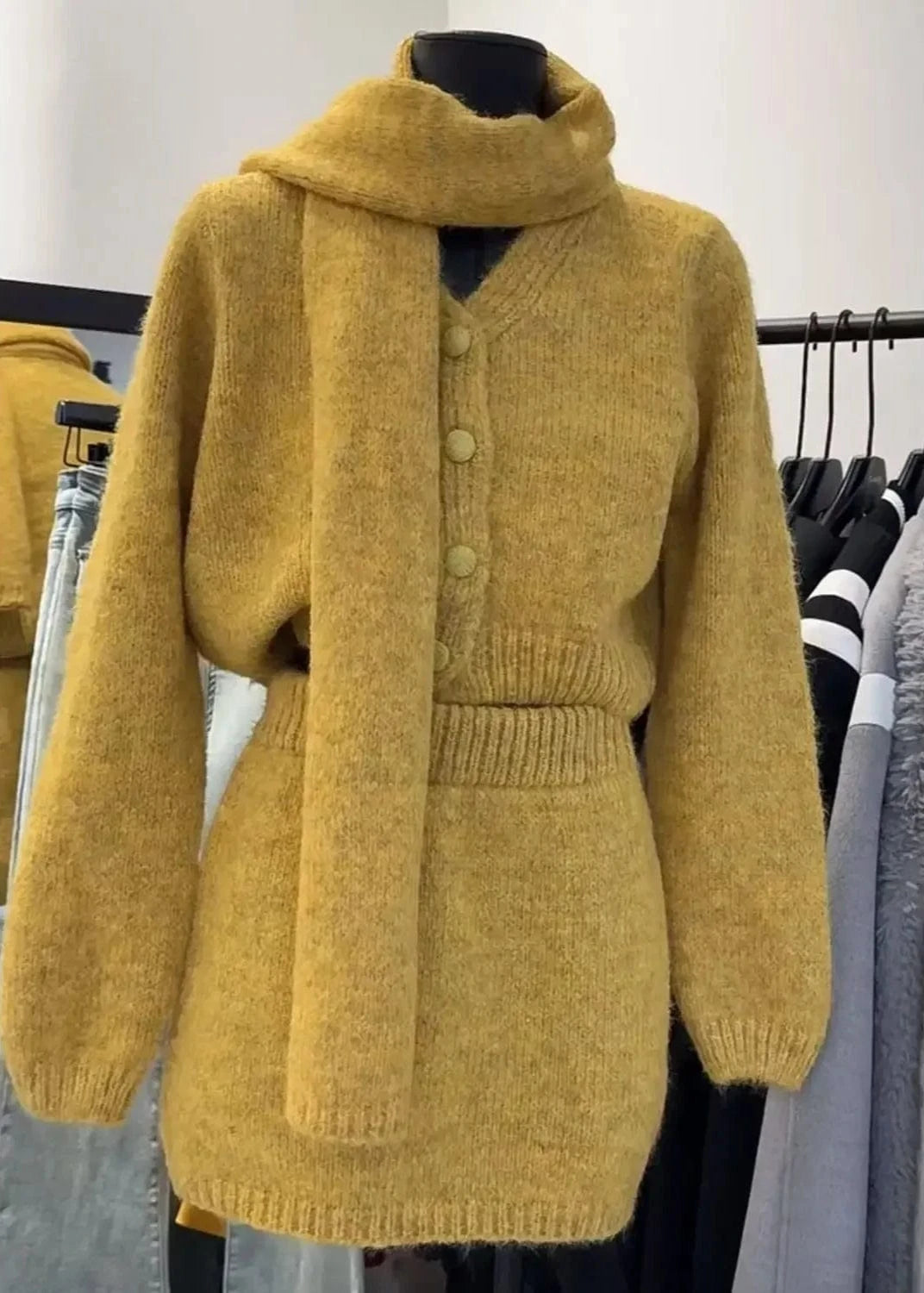 Mustard yellow knitted cardigan on a mannequin against a clothing rack background