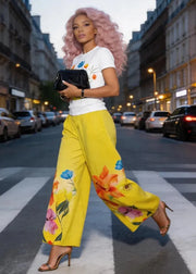 Woman in a city street wearing a white t-shirt with colorful designs and yellow floral pants.