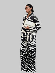Person wearing a zebra print outfit with a white bag, standing outdoors with 'Trafza' branding.