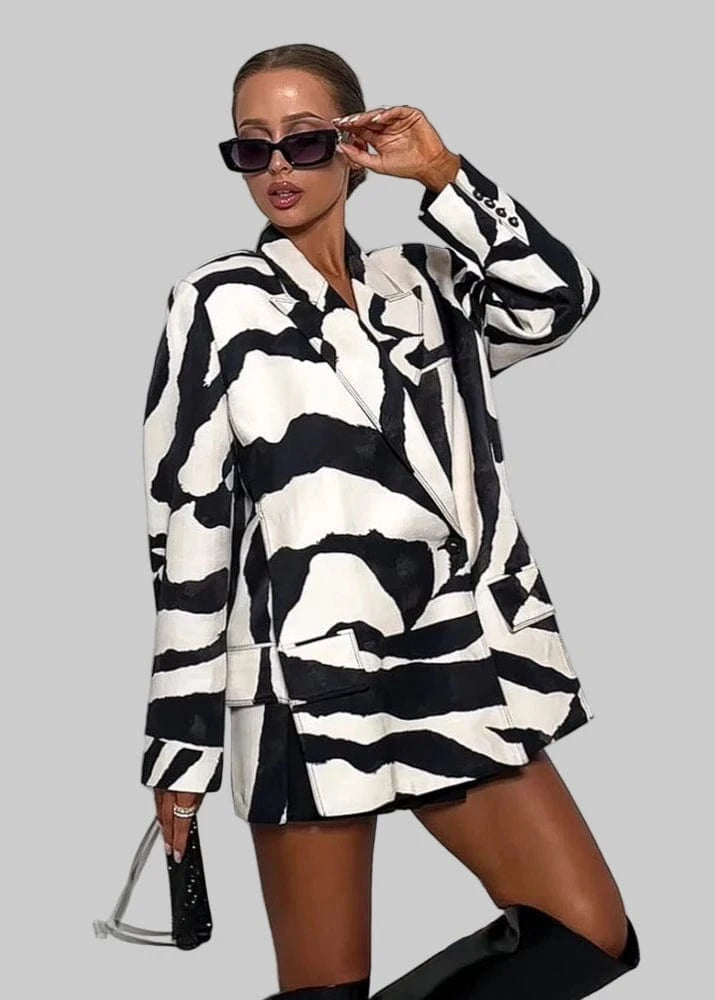Person wearing a black and white patterned outfit with sunglasses, standing against a white background with 'Trafza' branding.
