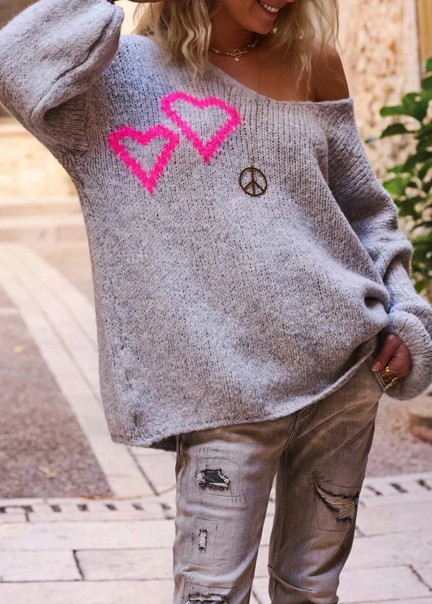 Person wearing a gray sweater with pink hearts and a peace symbol, standing outdoors.